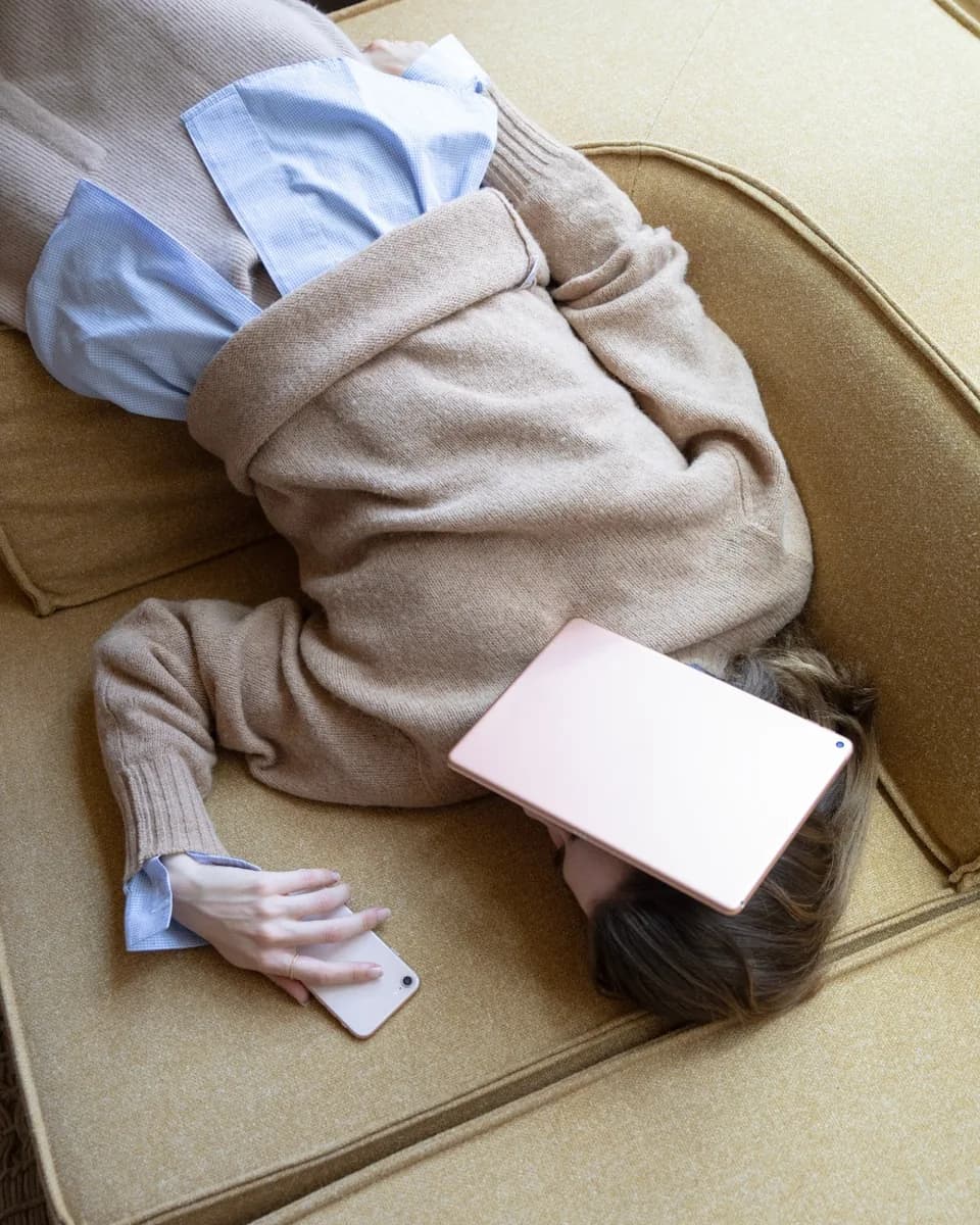 A woman lying face down on a sofa with a tablet resting over her face