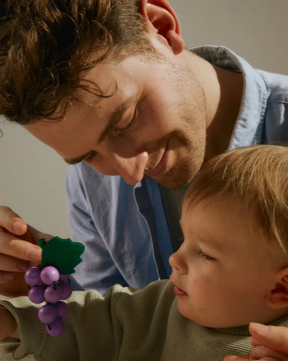 A man and a toddler playing with wooden toy fruit at a table