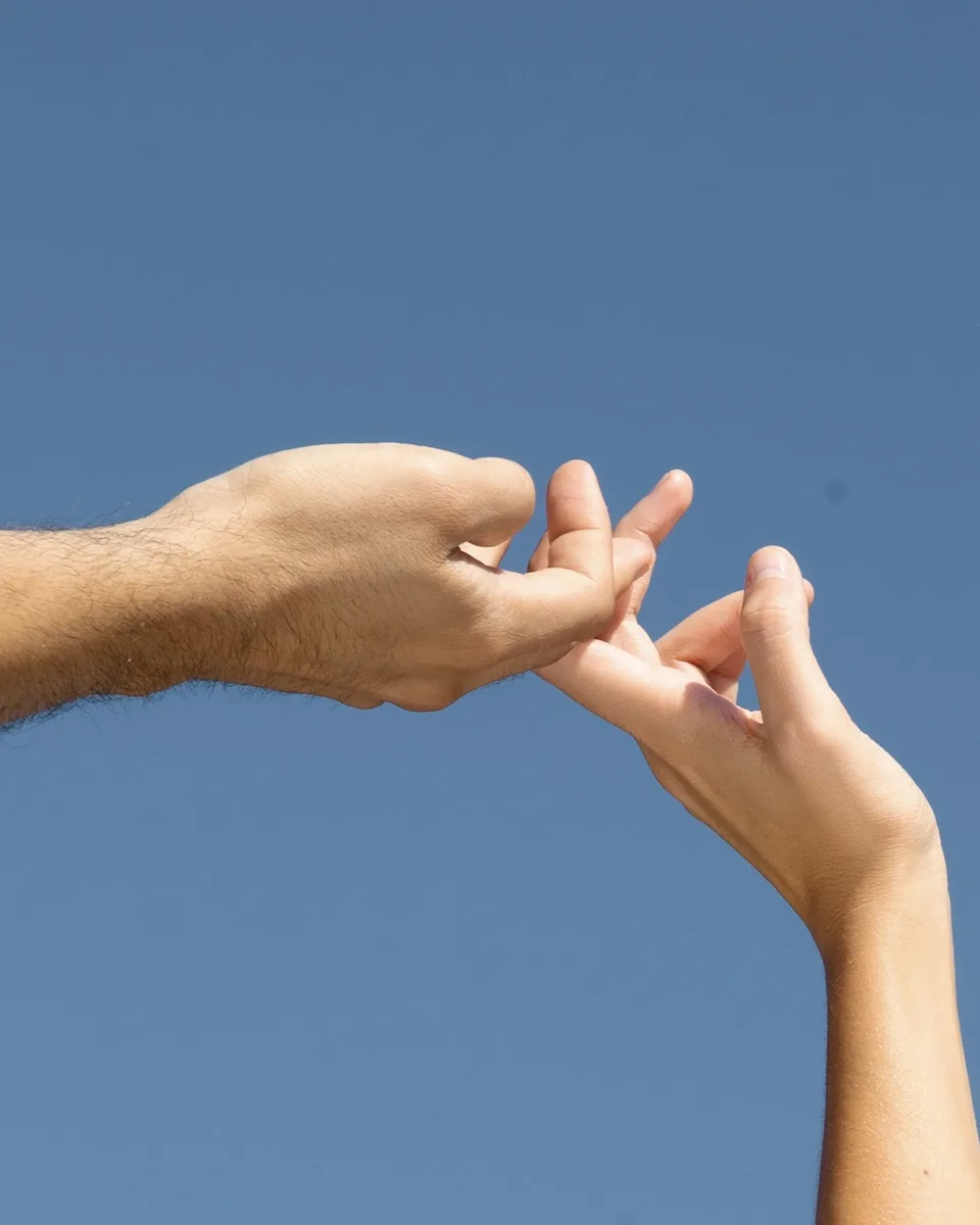 Two hands reaching toward each other against a clear blue sky
