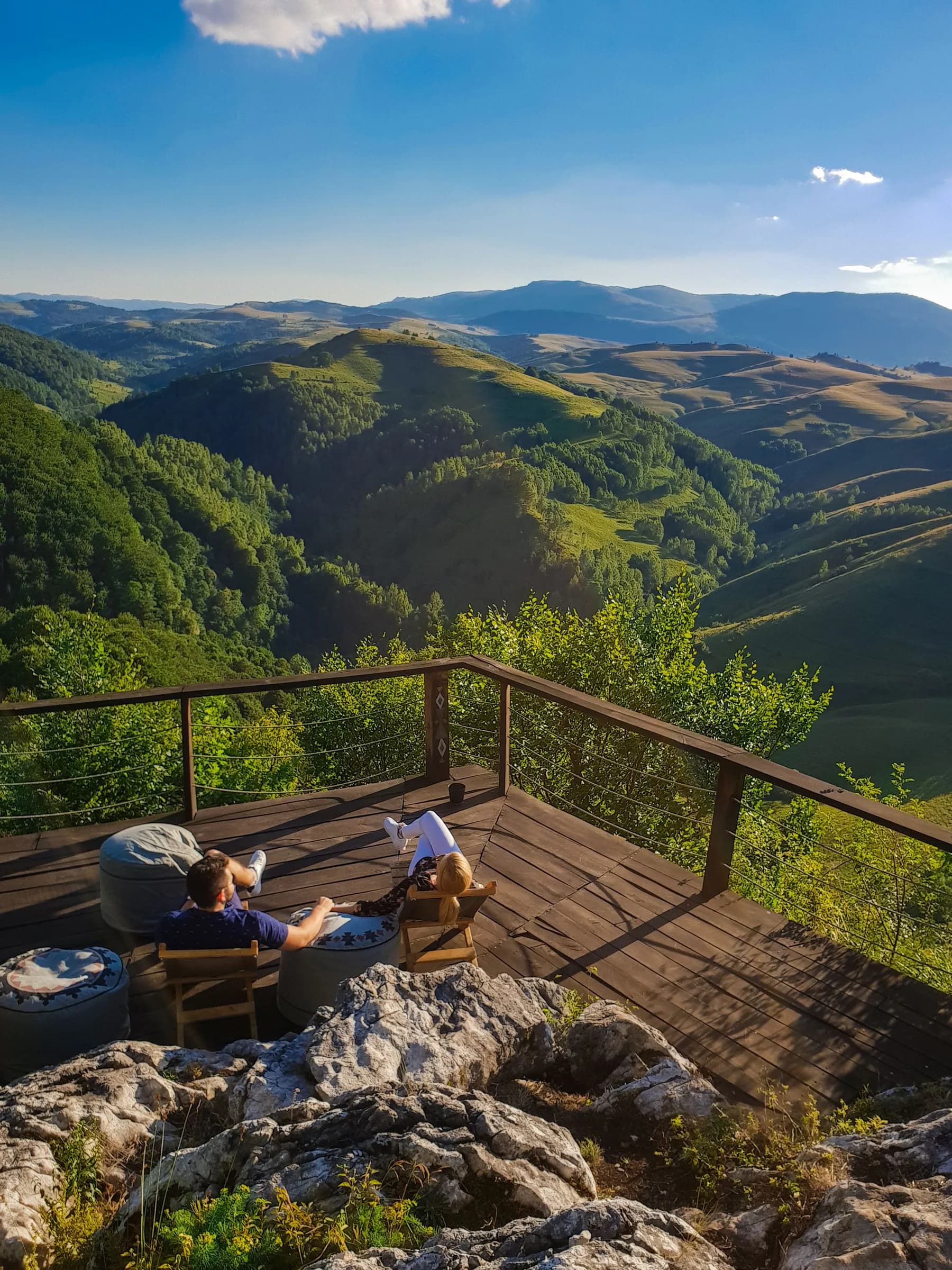 Two people relaxing on a deck overlooking green mountains