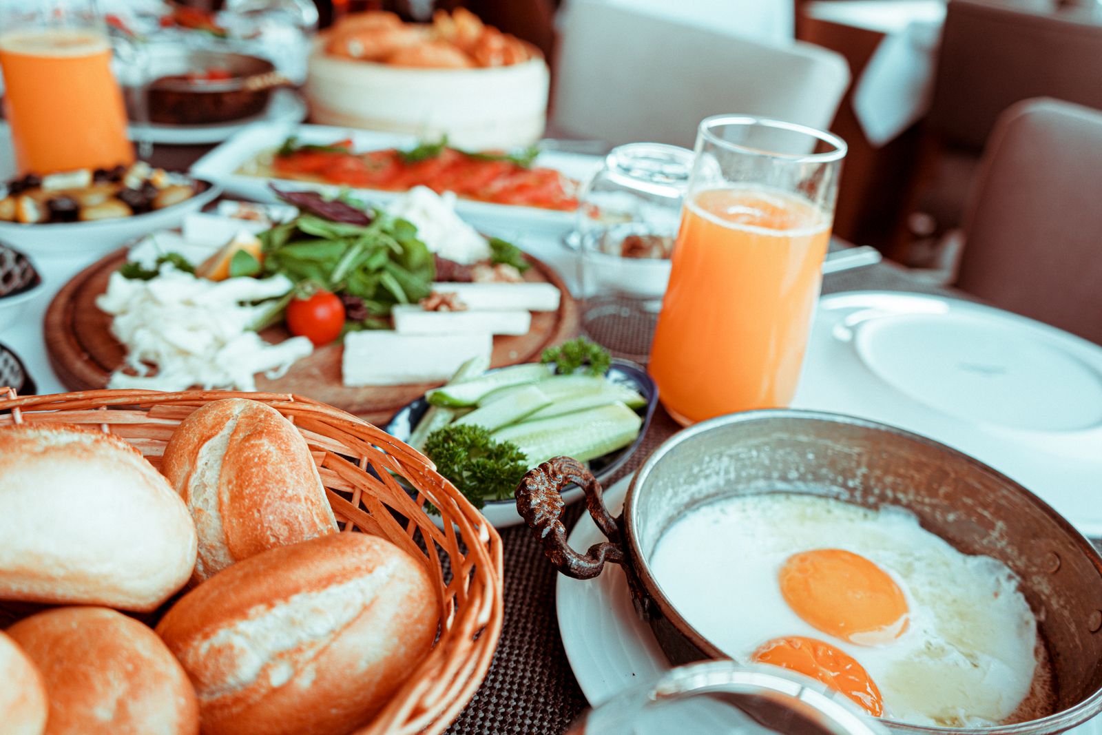 Breakfast table with fried eggs, fresh bread, vegetables, and orange juice