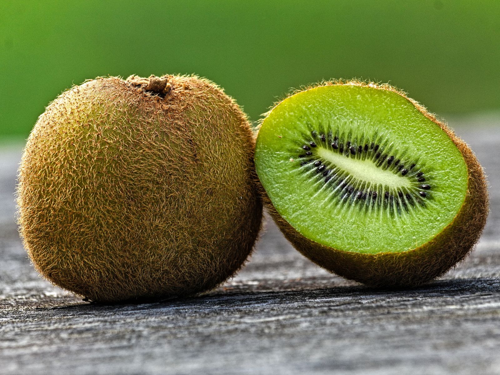 Whole and sliced kiwi fruit on a rustic wooden table