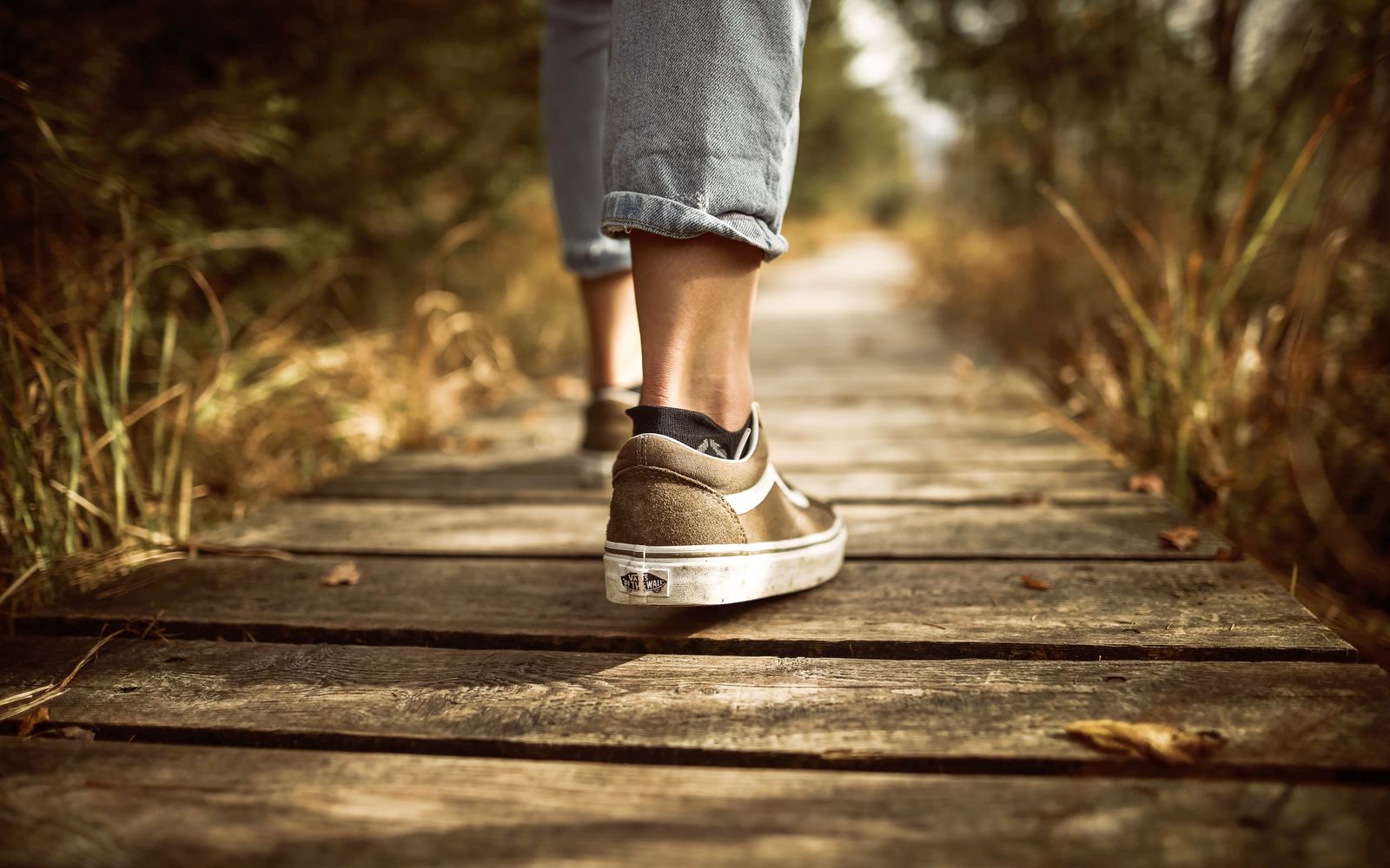 A person in sneakers walking along a sunlit outdoor path